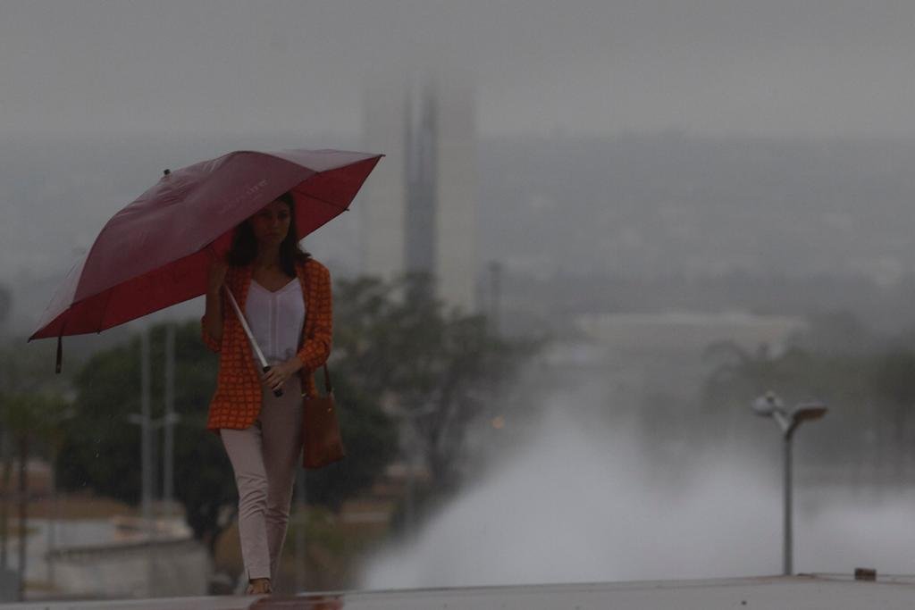 mulher com guarda chuva caminha na torre de tv com vista para o Congresso nacional