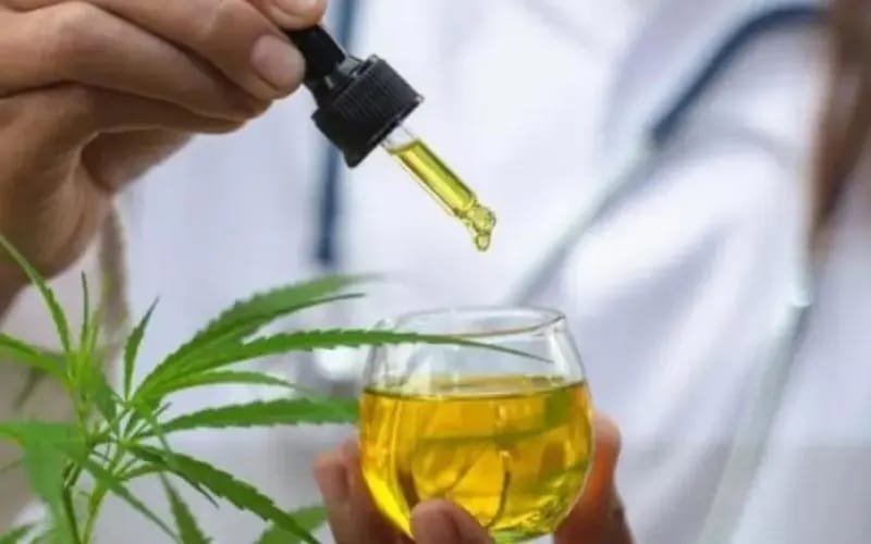 Foto de pessoa com jaleco segurando conta gotas com óleo de cannabis - Metrópoles
