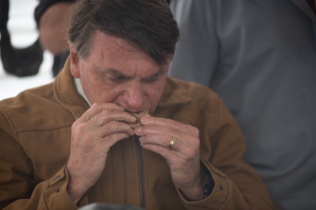 O presidente Jair Bolsonaro comendo churrasquinho em uma barraca no Guará, no DF