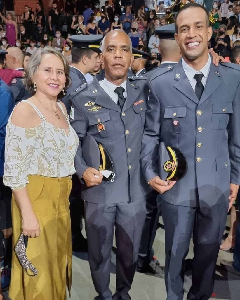 Soldado Anderson Araújo Costa Bomfim posa, de uniforme cinza, em formatura ao lado do pai e mãe