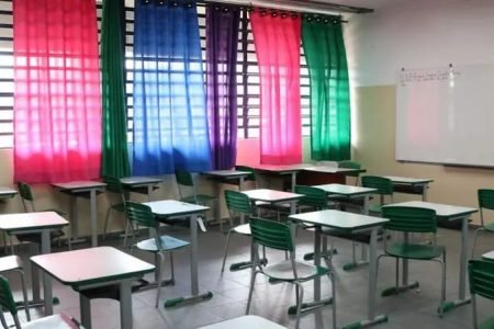 Imagem mostra sala de aula vazia com cadeiras verdes. As cortinas das salas são rosas, verdes, azuis e roxas - Metrópoles