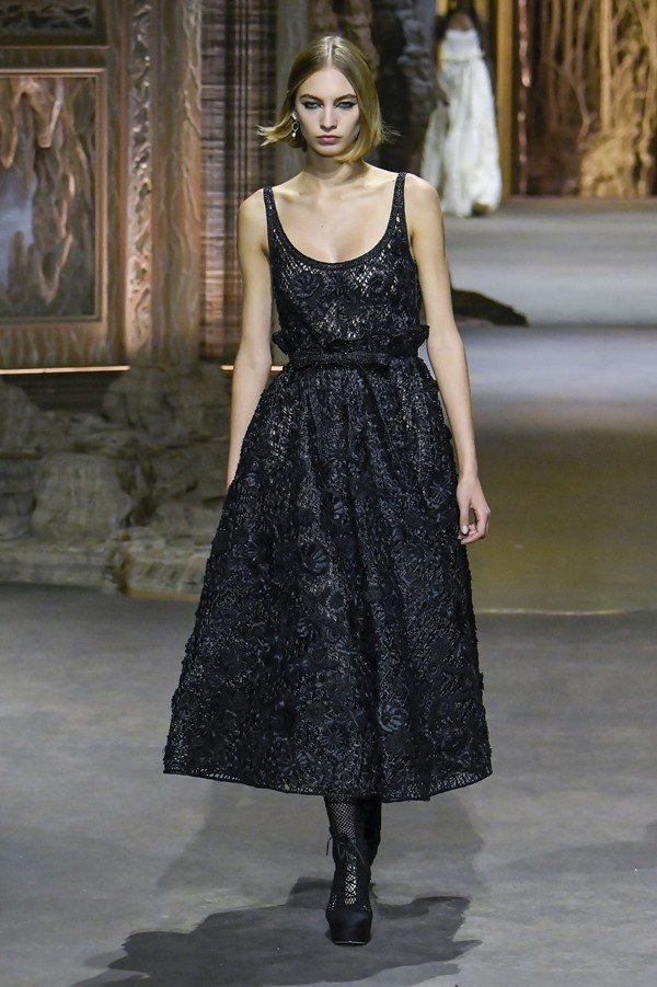 Uma modelo caminha na passarela durante o desfile de moda da Dior, coleção de Primavera/Verão 2023, como parte da Paris Fashion Week em 28 de setembro de 2022. A modelo é uma mulher branca de cabelo liso curto e loiro e usa um vestido longo preto de renda.