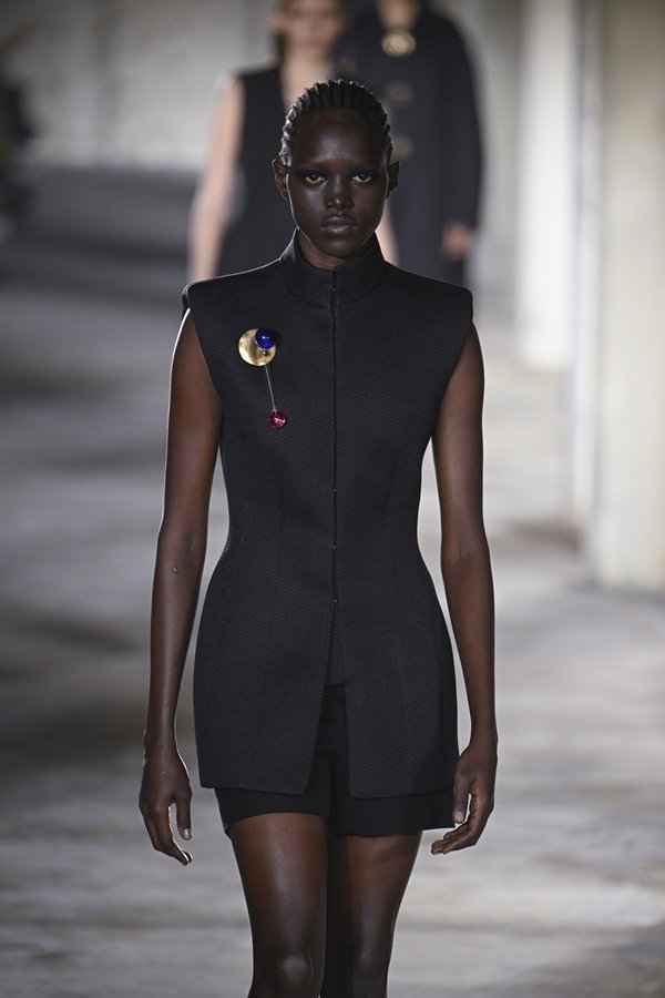 Uma modelo caminha na passarela durante o desfile de moda da Dries Van Noten, coleção de Primavera/Verão 2023, como parte da Paris Fashion Week em setembro de 2022. A modelo é uma mulher negra e jovem, de cabelo trançado curto, e usa um vestido preto que lembra um colete.