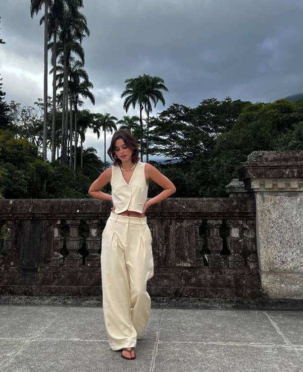 Influencer Luíza Nunes usando look de alfaitaria bege, com colete de botões