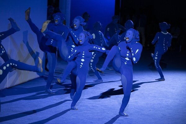 Homens e mulheres usando macacões azul, e uma pintura de rosto da mesma cor, dançando na abertura do desfile da marca Off-White, na Semana de Moda de Paris, em setembro de 2022