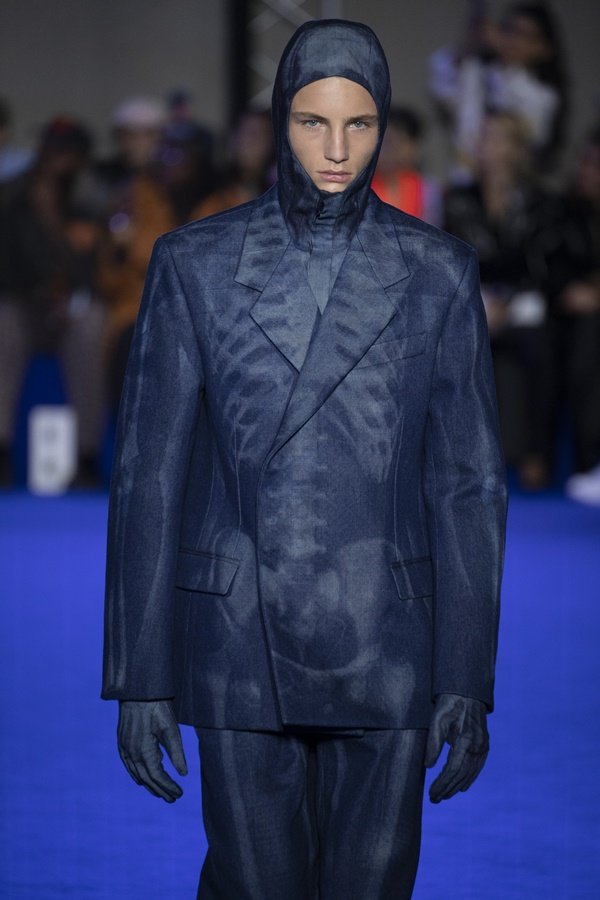 Um modelo caminha na passarela durante o desfile de moda da marca Off-White, coleção de Primavera/Verão 2023, como parte da Paris Fashion Week em setembro de 2022 em Paris, França. O modelo é um homem branco que usa um blazer estilo jeans com a estampa de um raio-x de um tórax. 