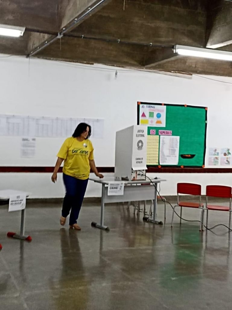 Fotografia colorida de mulher ao lado de cabine de votação