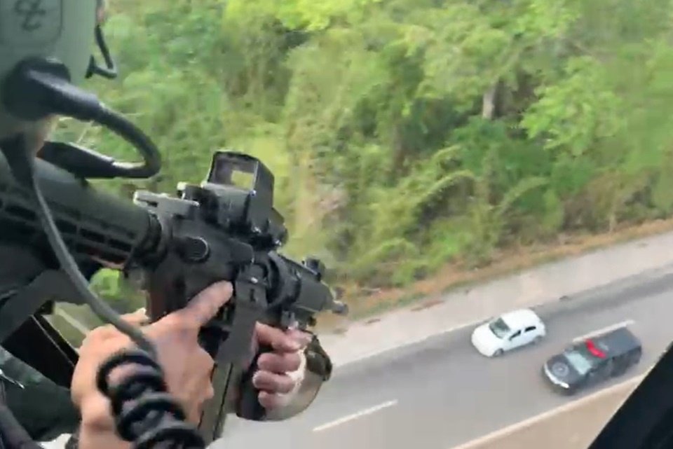 Policial em helicóptero aponta arma para carro em pista abaixo