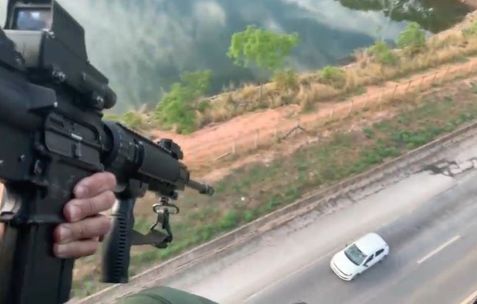 Policial em helicóptero aponta arma para carro em pista abaixo