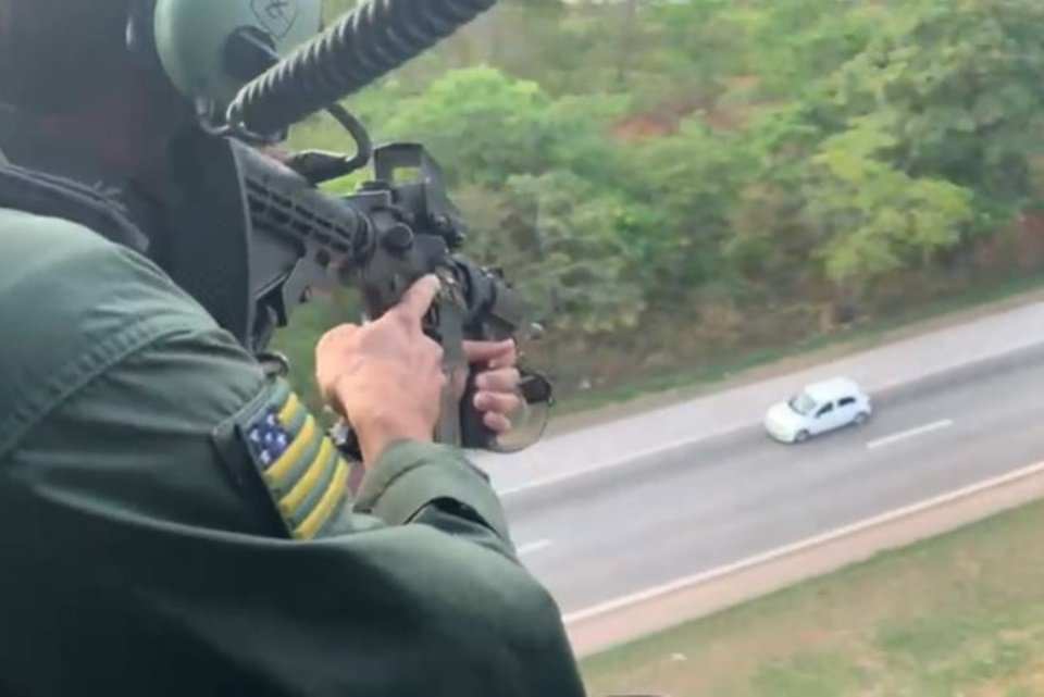 Policial em helicóptero aponta arma para carro em pista abaixo