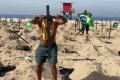 foto colorida de homem fincando cruz de madeira preta na areia da praia de Copacabana