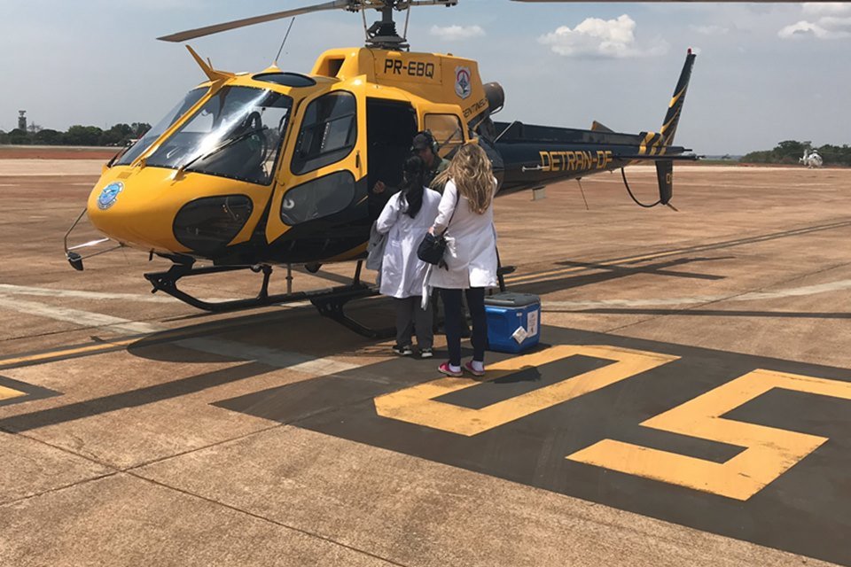Helicóptero amarelo e preto no chão e pessoas andando com mala