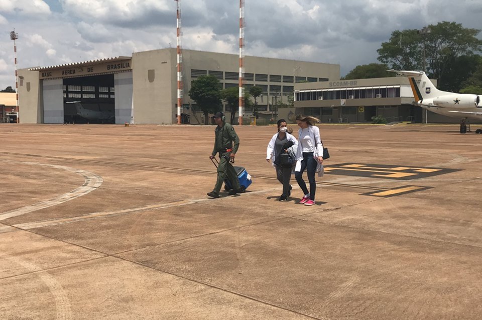 Helicóptero amarelo e preto no chão e pessoas andando com mala