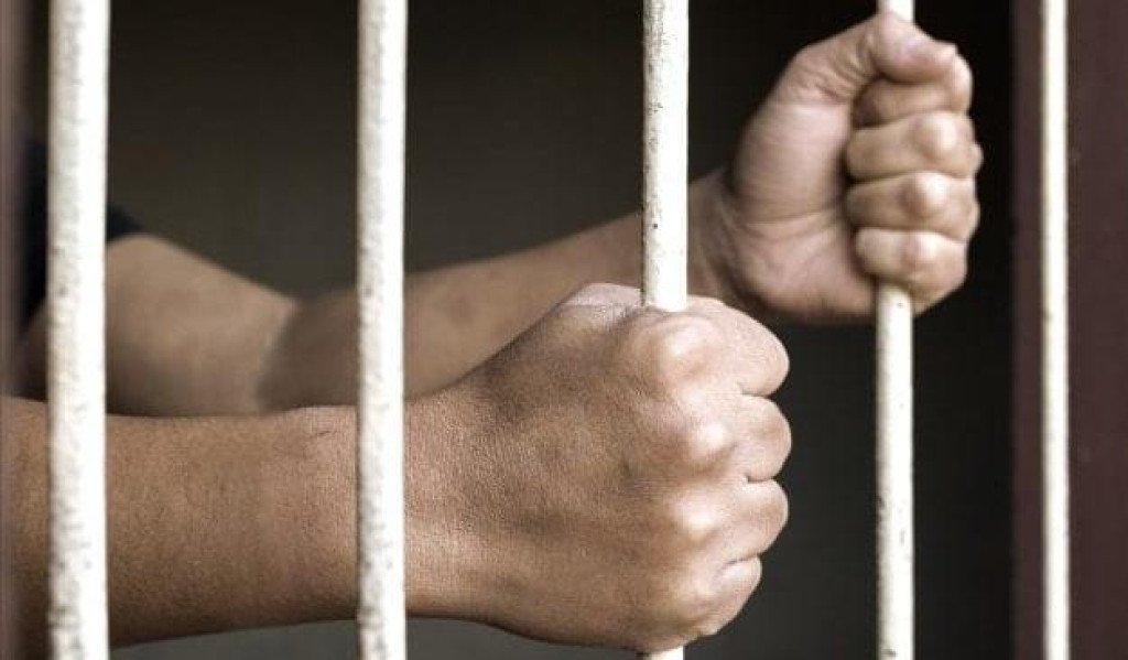 mãos de homem branco segurando barras de cela de prisão