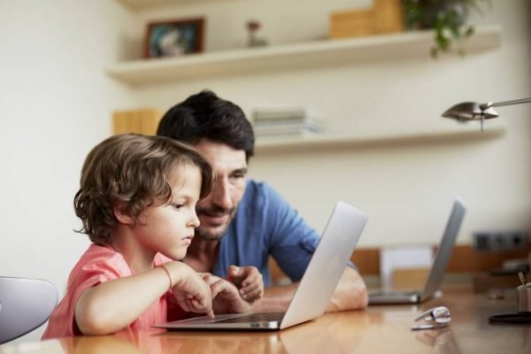 Man assisting son in using laptop