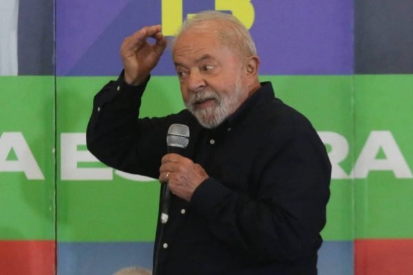 Foto colorida do presidente eleito Luiz Inácio Lula da Silva (PT). Na imagem ele fala em um microfone e acena com a mão direita sobre a cabeça. / Metrópoles
