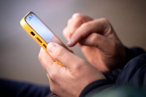 Homem branco mexendo no celular com capa amarela - Metrópoles