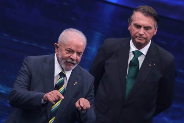 Lula e Bolsonaro, candidatos à presidência, em debate promovido pela TV Bandeirantes no segundo turno das eleições. Na foto, Bolsonaro aparece atrás de Lula ouvindo o ex-presidente falar e gesticular em resposta a pergunta - Metrópoles