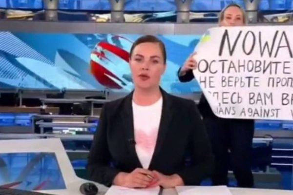 Frame mostra jornalista apresentando jornal russo em primeiro plano e atrás dela, outra colega com um cartaz anti-guerra criticando a ofensiva da Russia contra a Ucrânia - Metrópoles