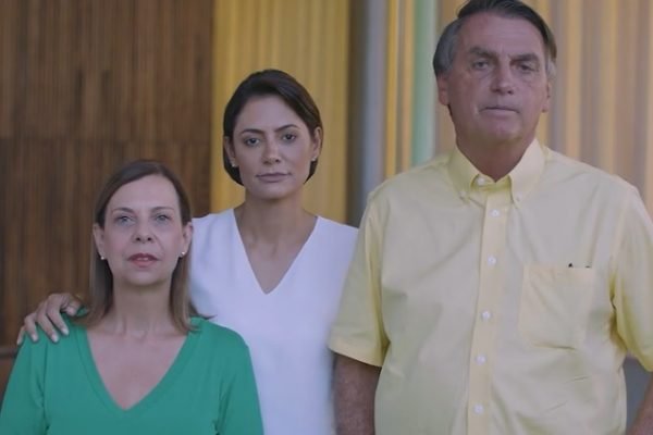 Em vídeo, Bolsonaro aparece ao lado da esposa, Michelle, e de mulher venezuelana pedindo desculpas por sua fala sobre prostituição de meninas do país. Ele usa camisa amarela e as mulheres, verde e branca - Metrópoles