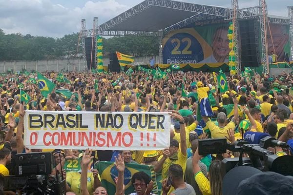Ato de campanha de Jair Bolsonaro em São Gonçalo, no Rio de Janeiro, onde levanta-se faixa que diz "Brasil não quer o comunismo". Na foto, eles comemoram usando verde e amarelo diante do palco com autoridades - Metrópoles
