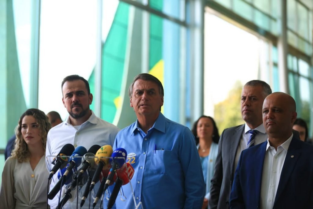 O presidente e candidato à reeleição Jair Bolsonaro caminha no Planalto em ato com apoio de políticos goianos. Ele usa camisa azul com adesivo de campanha, diante de pulpito com microfones - Metrópoles