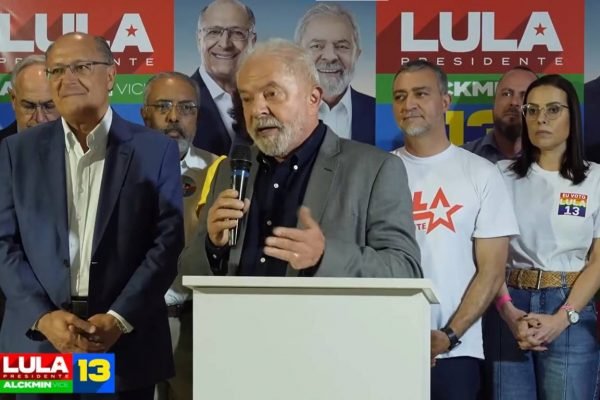 Lula faz campanha no Rio Grande do Sul e discursa ao lado de aliados e o candidato a vice-presidente, Geraldo Alckmin. Ele segura microfone diante de pulpito branco - Metrópoles