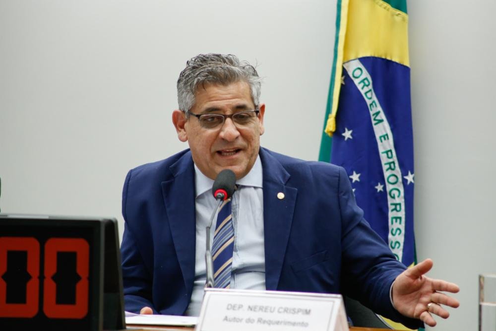 Deputado Nereu Crispim (PSD-RS), que não foi reeleito em 2022, fala em sala de comissão diante de microfone e bandeira do Brasil atrás - Metrópoles
