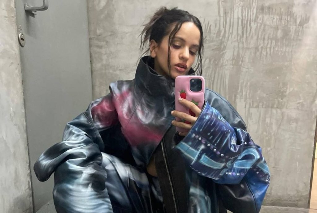 A cantora espanhola Rosalía tira selfie com um casaco e calça oversize da mesma estampa e cabelo preso - Metrópoles