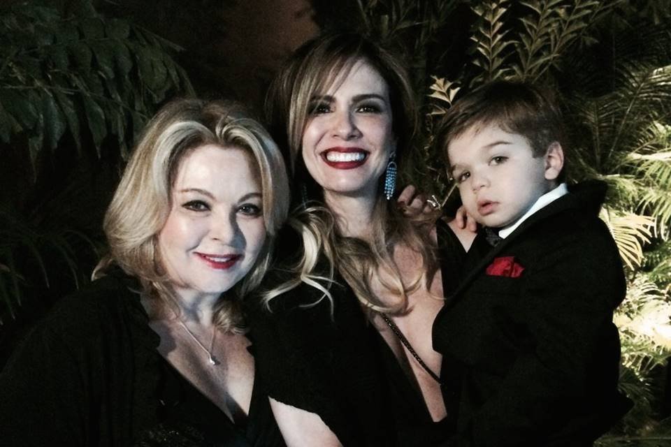 Luciana Gimenez e a mãe, Vera Gimenez, junto a criança no colo da apresentadora. Ela usam preto e sorriem para foto - Metrópoles