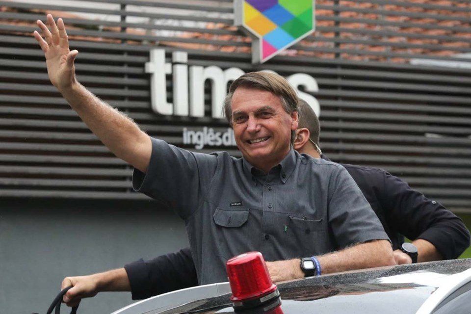 Bolsonaro ao lado de lutadores que declararam apoio à sua campanha em São Paulo. Ele acena e sorri de cima de um carro, acompanhado por uma comitiva - Metrópoles
