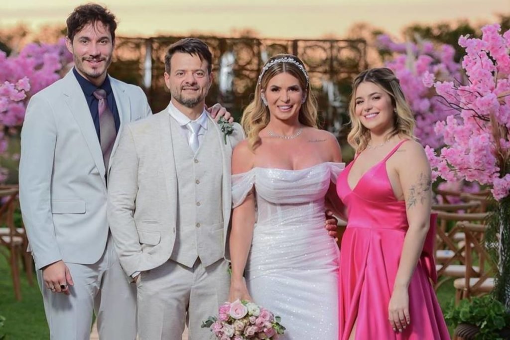 Dois homens de terno, uma mulher vestida de noiva e uma mulher de vestido rosa posam um ao lado do outro