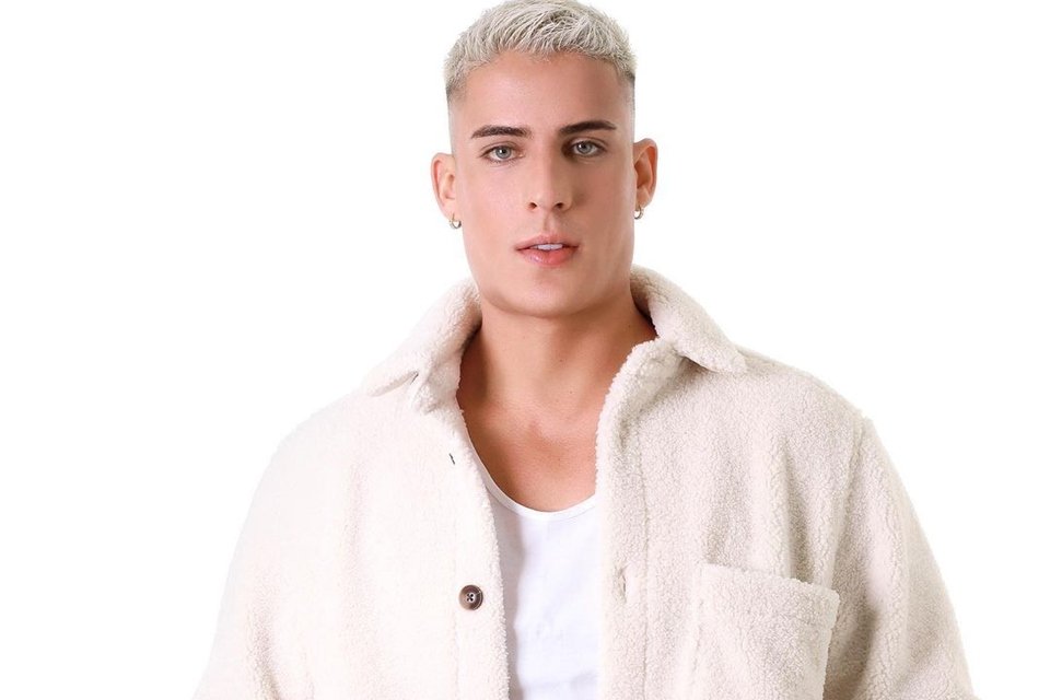 Foto colorida de Tiago Ramos usando jaqueta em fundo branco e com o cabelo platinado - Metrópoles