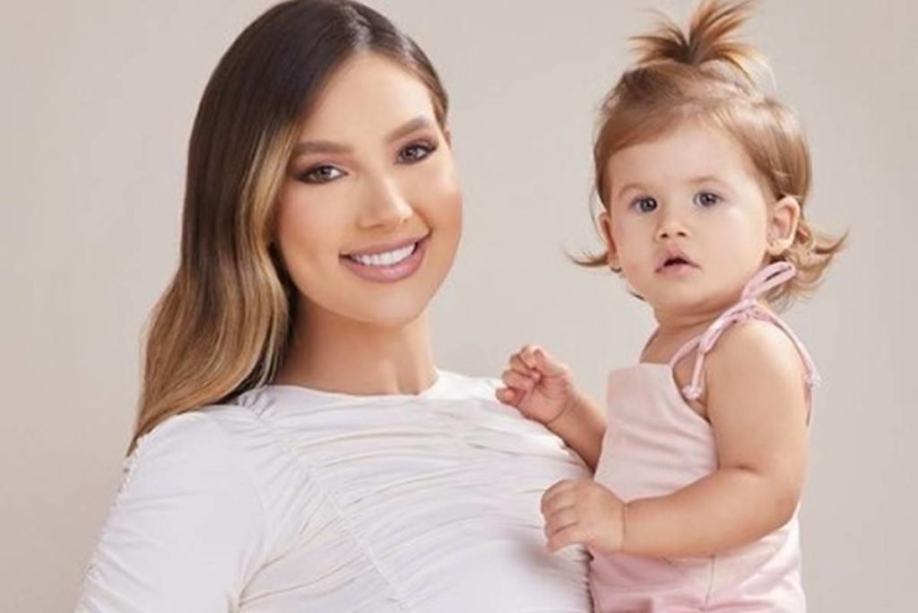 A influenciadora Virgínia com sua filha no colo, sorrindo. Ambas usam roupas claras - Metrópoles