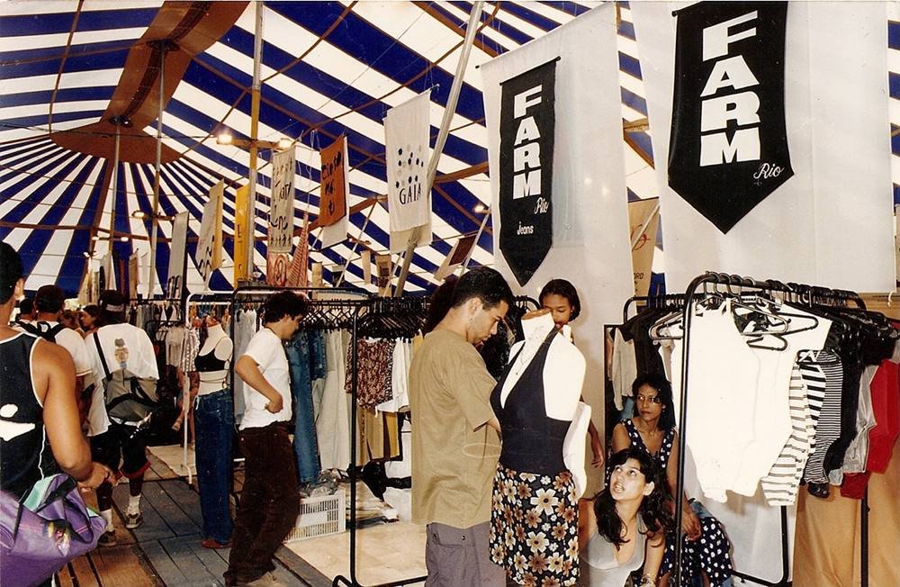 Pessoas comprando e expondo produtos na Babilônia Feira Hype, no ano de 1997. Um dos expositores é a marca Farm, ainda no começo de sua fundação