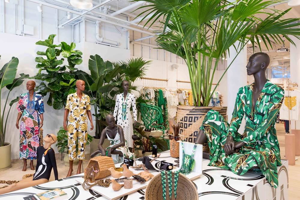 Parte interna da loja da marca Farm em Nova York. O espaço possui plantas como palmeiras e manequins vestindo roupas estampadas, com desenhos em homenagem à fauna e à flora brasileira