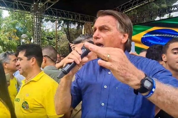 O presidente e candidato à reeleição Jair Bolsonaro discursa com microfone na mão em evento na cidade de Teófilo Otoni (MG). Várias pessoas o cercam e uma bandeira do Brasil aparece no telão atrás - Metrópoles