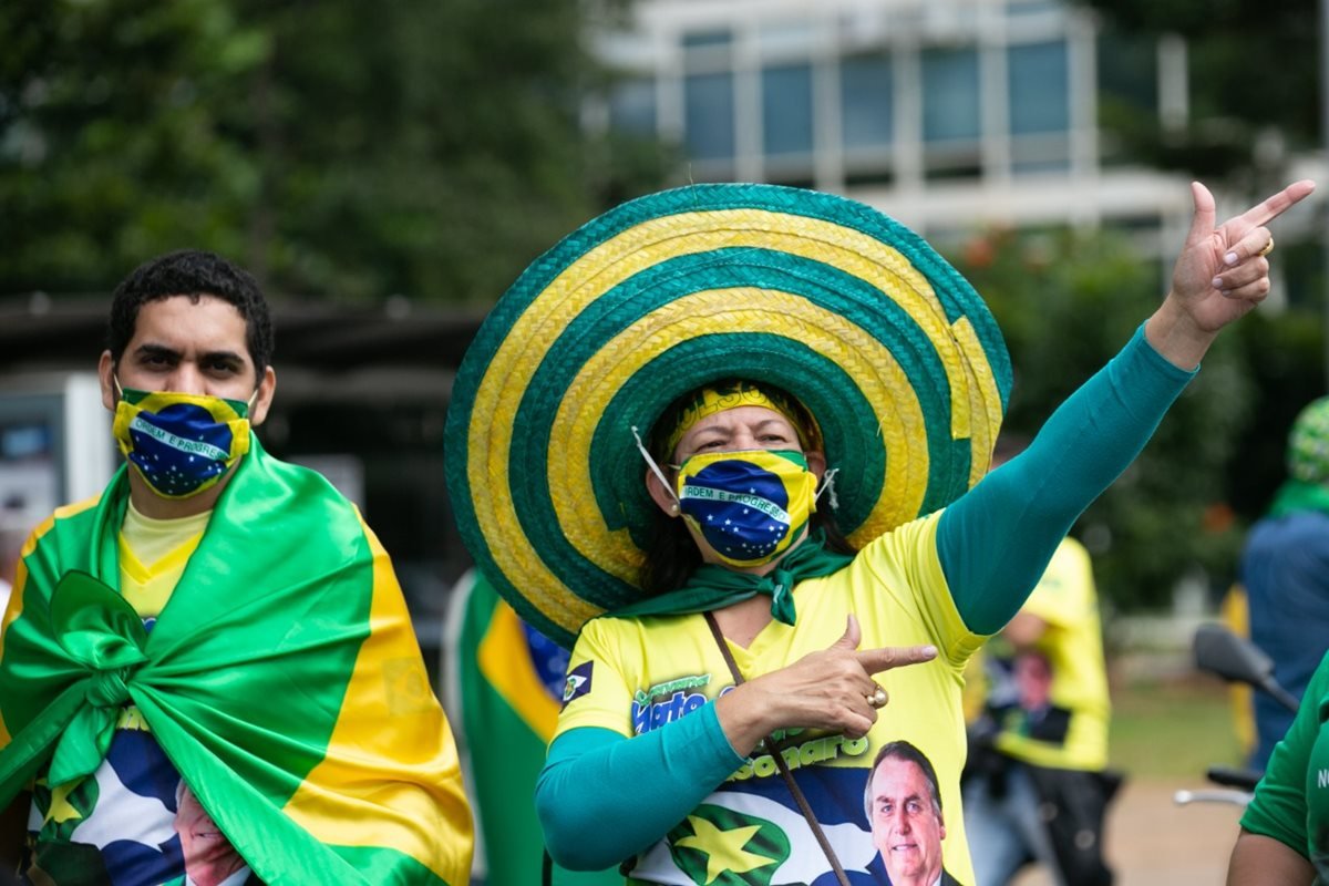 Mulher e homem, ambos brancos com cabelos castanhos, em manifestaçaõ pró-Bolsonaro na Esplanada dos Ministérios, em Brasíli. Eles usam máscara com estampa da bandeira do Brasil e roupas nas cores verde e amarelo, além de uma camiseta com o rosto do presidente Jair Bolsonaro estampado