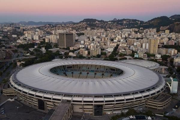 Estádio Maracanã, no Rio de Janeiro, visto de cima. Ele é rodeado por prédios e ao fundo um morro ao entardecer - Metrópoles