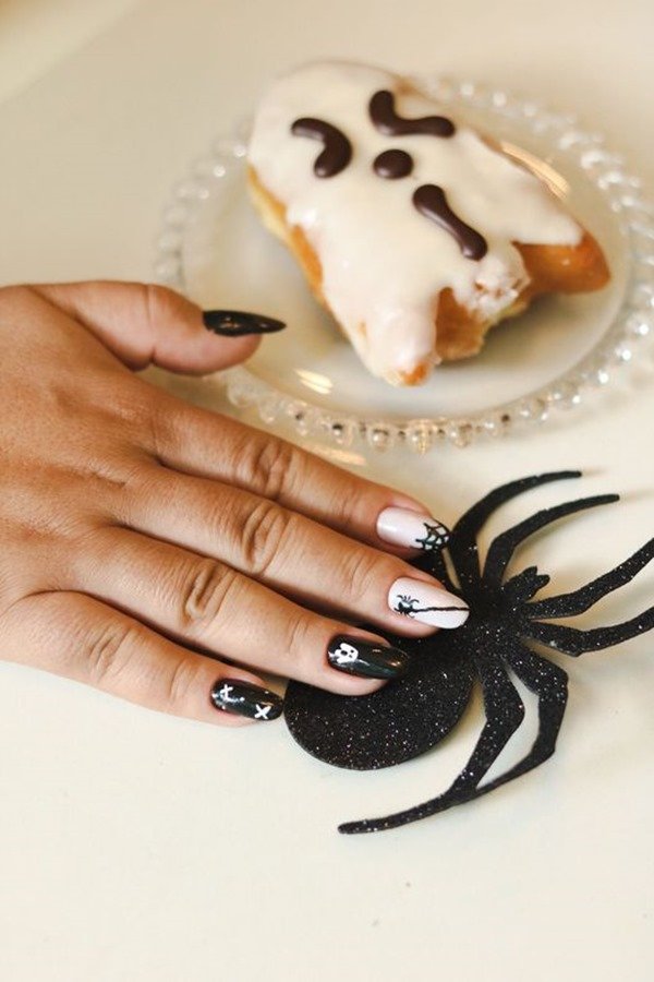 Foto colorida de uma mão feminina comum biscoito em formato de fantasma ao lado e um recorte de aranha abaixo da mão