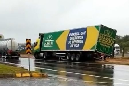 foto colorida de caminhão verde e amarelo atolado em rodovia