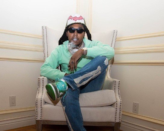 Rapper Takeoff sentado usando casaco verde e boné branco - Metrópoles