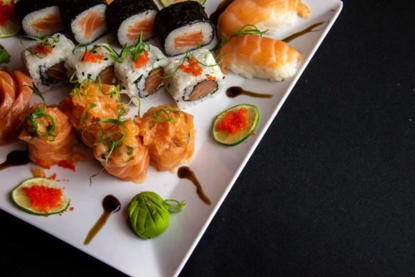 Na foto, fundo preto com prato branco e vários elementos da culinária japonesa - Metrópoles