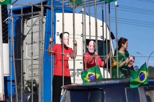 Foto mostra crianças com máscaras do presidente eleito Lula e do ministro do STF, Alexandre de Moraes, presas em jaulas sob caminhão em manifestação bolsonarista, na cidade de Balenário Camboriu (SC). Várias bandeiras do Brasil adornam o local - Metrópoles
