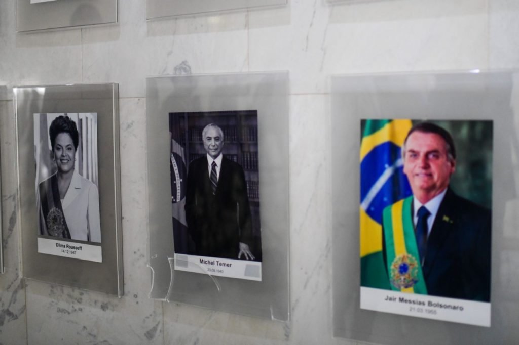 Retrato do ex-presidente Michel Temer, ao lado de DIlma e Bolsonaro no palacio do planalto, cai e tem uma de suas pontas quebradas - Metrópoles