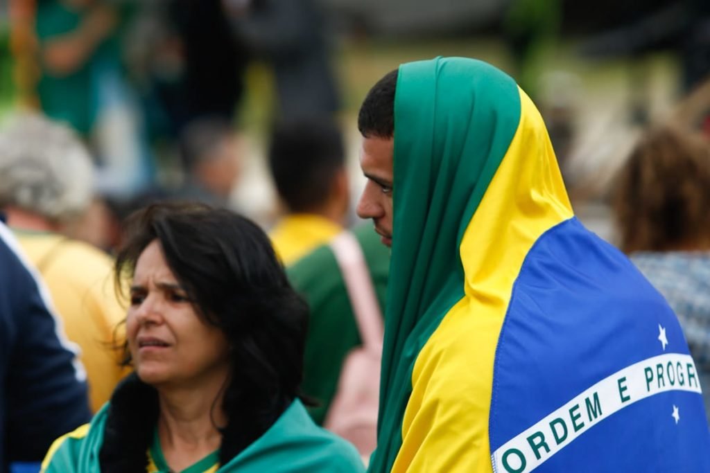 Manifestantes pró-Bolsonaro com bandeira do brasil na cabeça e semblante triste em frente ao Quartel General do Exército Forte Caxias, QG do exército em Brasília - Metrópoles