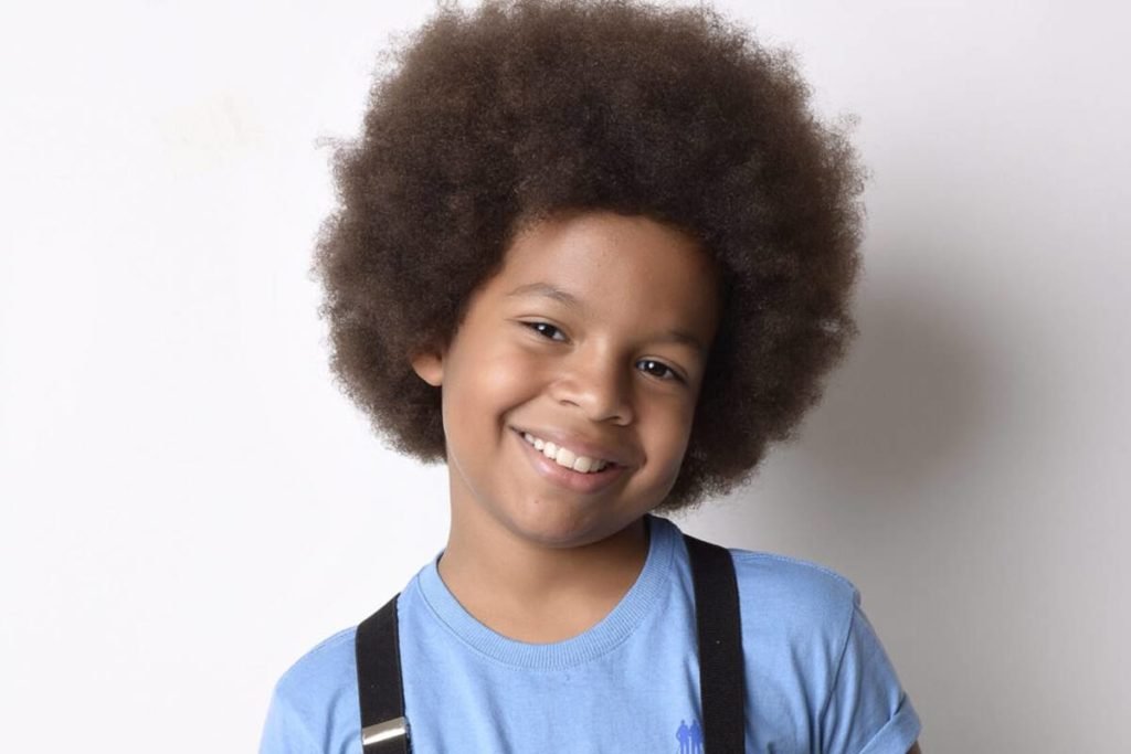 Foto colorida do ator mirim Levi Asaf. Criança negra de cabelo black power, veste uma blusa azul - Metrópoles