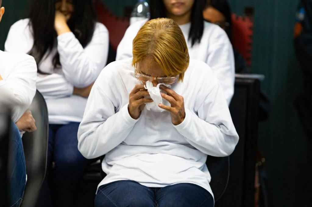 A ex-deputada e cantora gospel Flordelis, acusada de matar o marido, durante julgamento frente à mesa julgadora. Ela usa cabelo curto e loiro, moletom e aparece sentada assoando o nariz - Metrópoles