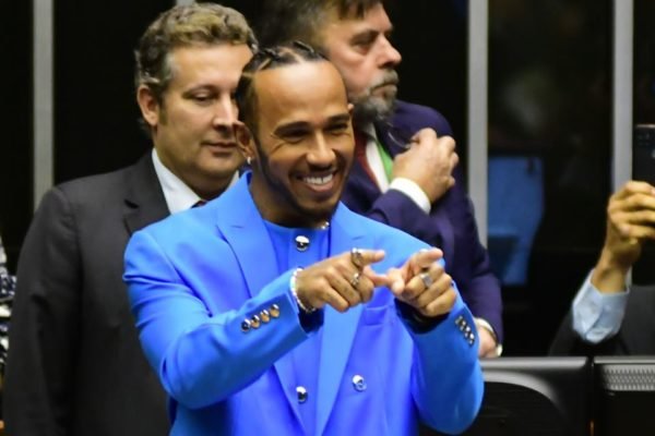 O piloto britânico Lewis Hamilton na Câmara dos Deputados para receber título de cidadão honorário do Brasil. Na foto, ele sorri e aponta para frente no plenário da casa legislativa - Metrópoles