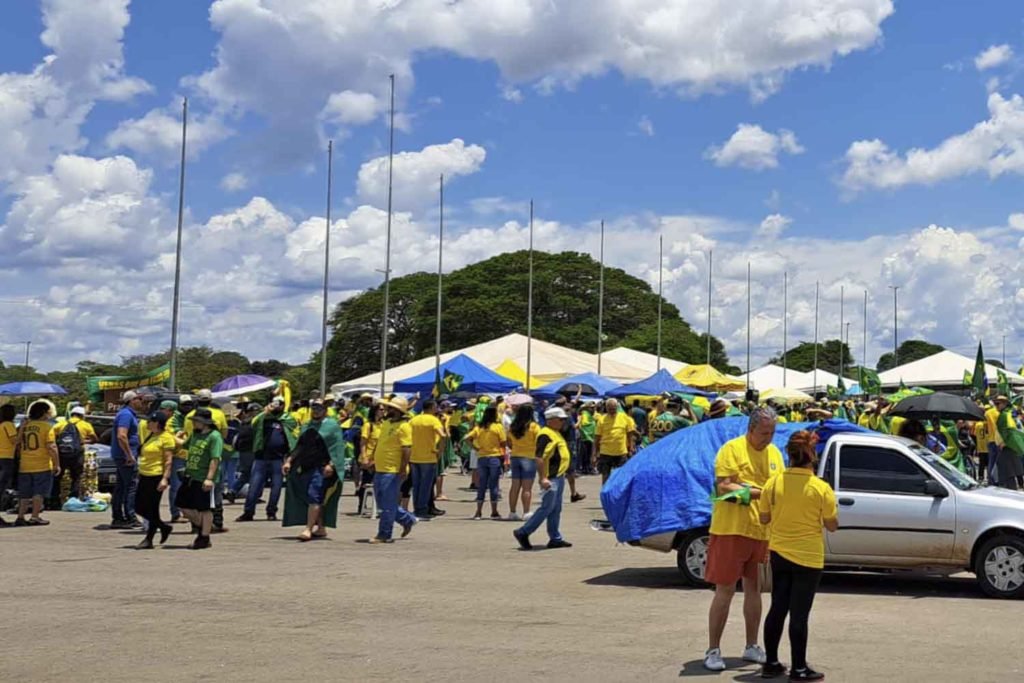 Apoiadores do presidente derrotado nas eleições Jair Bolsonaro com camisas amarelas e barracas com bandeiras do Brasil no QG do Exército, em Brasília. O céu está azul e com nuvens - Metrópoles